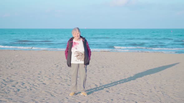 Elderly Woman Stands on Sea Beach Against Waves at Sunset
