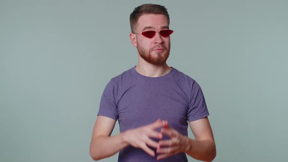 Seductive Cheerful Stylish Man in Purple Tshirt Wearing Sunglasses Charming Smile on Gray Wall