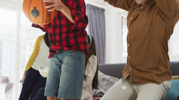 Excited asian parents with daughter and son on couch with basketball watching sport on tv, cheering