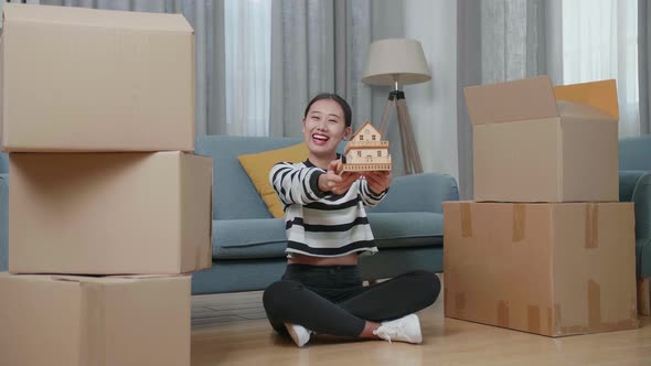 Asian Woman With Cardboard Boxes Smiling And Showing House Model To Camera In The New House