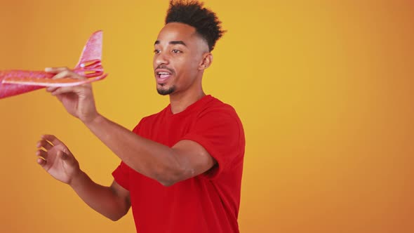 Funny Adult Black Man Playing with Toy Airplane on Orange Studio Background