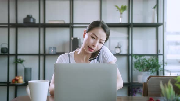 busy asian female mother working with laptop and smartphone at dining table