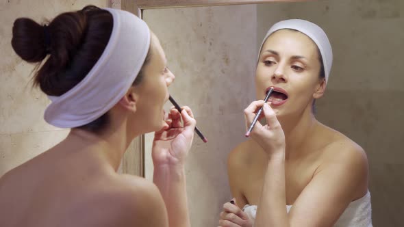 Beautiful Young Woman Putting Red Lipstick and Looking in Mirror. 