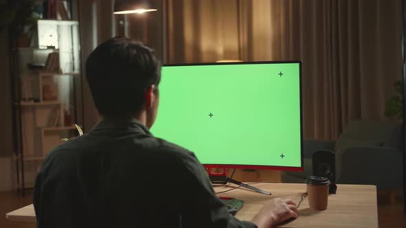 Asian Male Works With Mock Up Green Screen Computer Display. He Works At Night