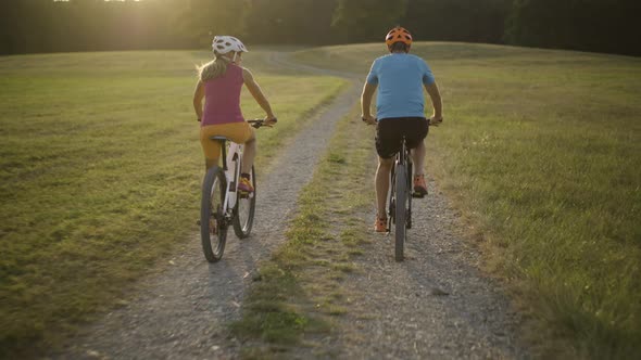 Following Couple Cycling on Gravel Path Through Grassland