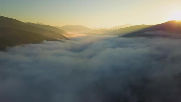 Aerial view of vibrant sunset over white dense foggy clouds with distant dark silhouettes of