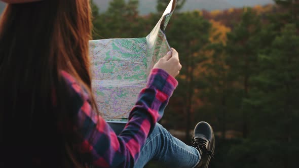 A Young Woman is Sitting on a Rock and Holding a Map in Her Hands