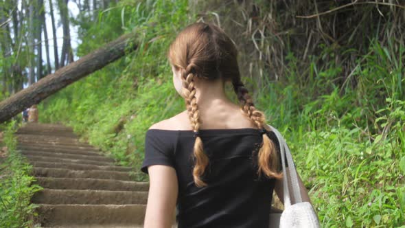 Lady Walks Up Old Brown Stairs Between Green Bushes