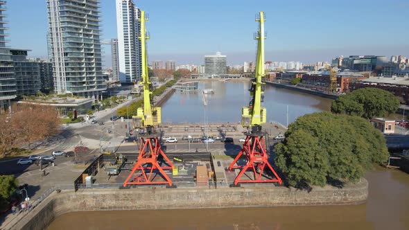 Aerial view of a waterway flying between two cranes over a bridge at Buenos Aires city