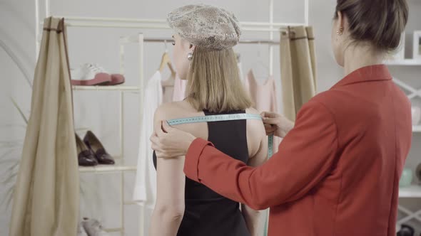 Back Angle View of Concentrated Dressmaker Measuring Shoulders of Slim Elegant Woman in Atelier