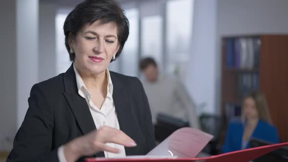 Portrait of Elegant Concentrated Caucasian Businesswoman Examining Documents and Looking at Camera