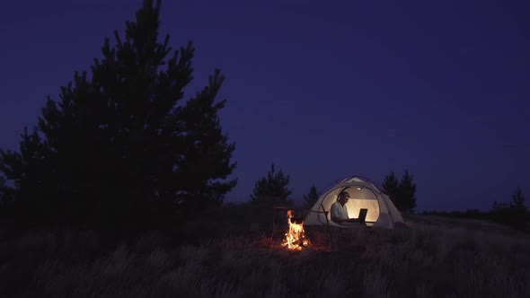 Freelancer Works Behind a Laptopin in a Tent Near a Fire