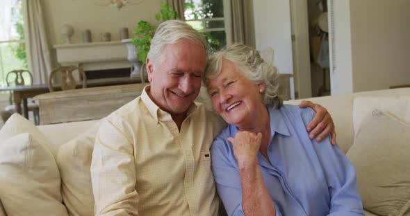 Portrait of smiling caucasian senior couple hugging each other while sitting on the couch at home