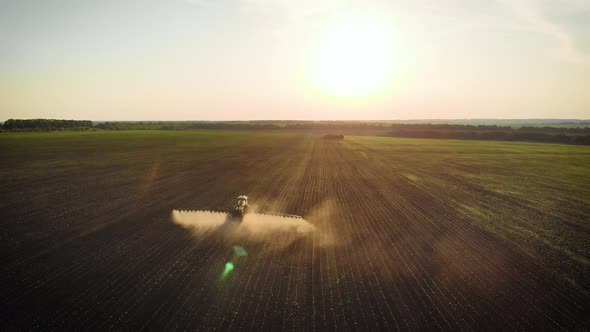 Aerial View of Farming Tractor Spraying on Field with Sprayer, Herbicides and Pesticides at Sunset