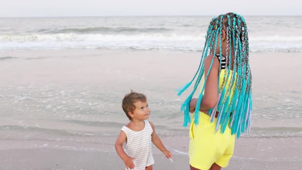 A Boy in a Striped Tshirt is Dancing to the Music with His Sister African Braids on the Beach Near