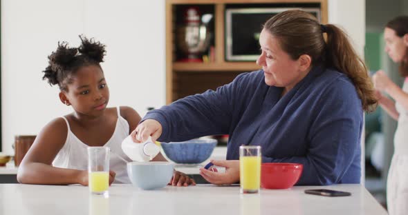 Happy caucasian lesbian couple and their african american daughter eating breakfast in kitchen