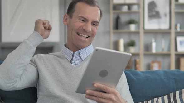 Relaxing Middle Aged Man Celebrating Success on Tablet