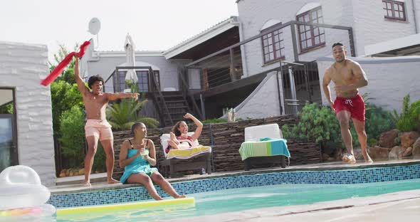 Latin man jumping into swimming pool and laughing with friends at pool party