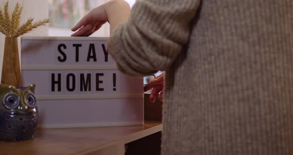 Woman walks in and Switches on Decorative Lightbox Written Stay Home in Comfy and Cozy Home