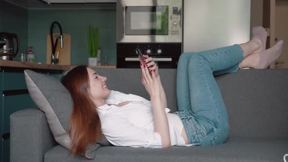 Girl Lying Relaxing on the Couch and Scrolling Using Her Smart Phone