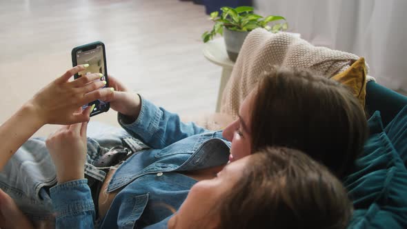 Young Women Sitting on Sofa and Watching Short Funny Videos Using Mobile Phone