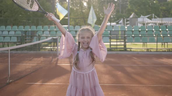 Cute Little Smiling Happy Girl with a Tennis Racket in Her Hands Standing on the Tennis Court