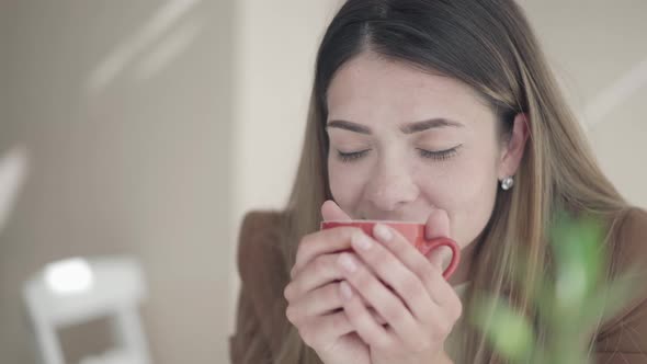 Closeup of Young Caucasian Woman Smelling Delicious Tea or Coffee and Smiling