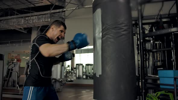 Slow Motion Footage of a Young Strong Tall Sportsman Punching Boxing Bag