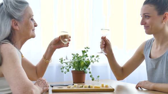 Female Portrait of Adult Daughter and Senior Mother Talking and Drinking Champagne at Home Sitting