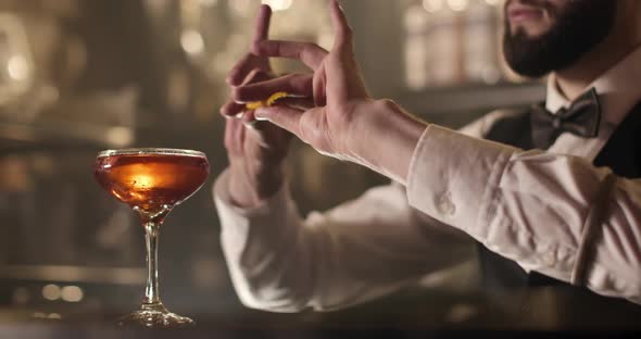 Close-up Shooting. The Bartender Is Squeezing Out a Piece of Orange Peel and Decorating the Cocktail