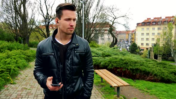 Young Handsome Happy Man Goes and Listen To Music From Earphone in Park