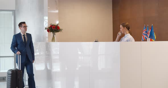Businessman Making Booking at Front Desk with Female Receptionist in Hotel Lobby