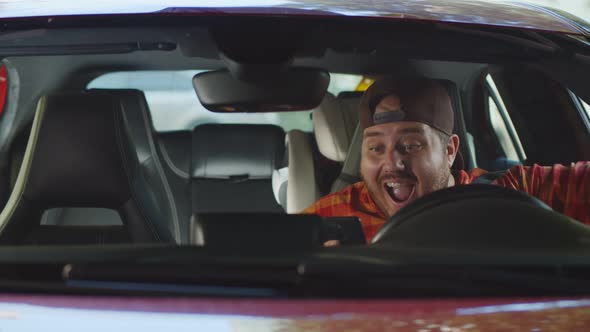 Young Fat Man Sitting in Driving Seat Inside Car Chatting on Smartphone and Smiling