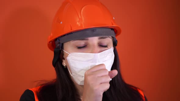 Female Construction Worker in Overalls and Medical Mask Coughing on Orange Background