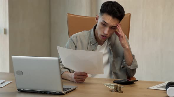 Young Asian Man Counts Money on Calculator Looking in Papers