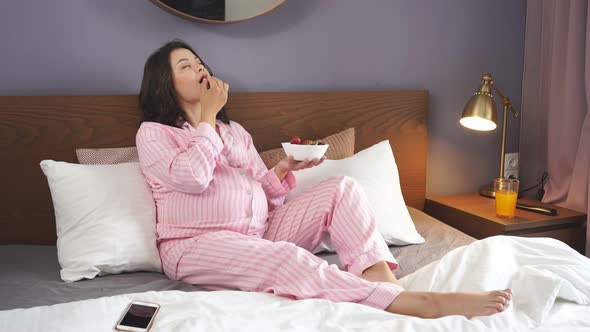 Pregnant Woman Eating Strawberries Sitting on Bed at Home.