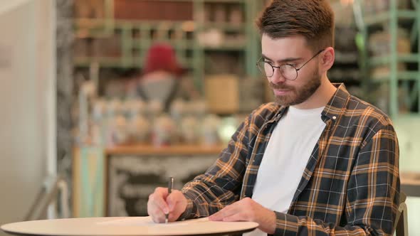 Focused Young Man Doing Paperwork in Cafe