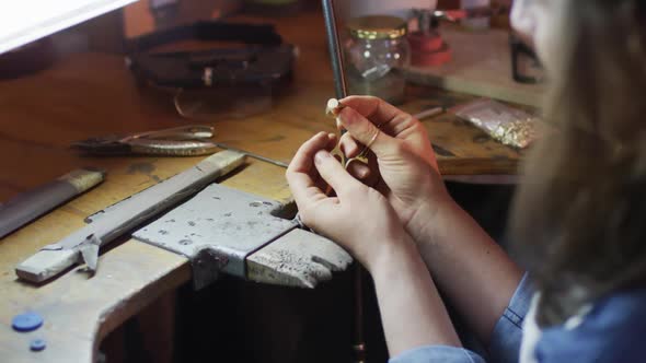 Close up of hands of caucasian female jeweller making ring in workshop