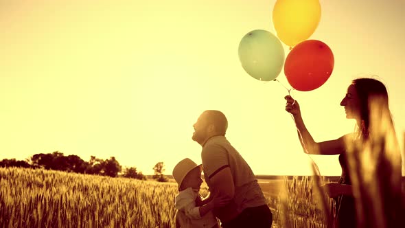 Mom is Standing in Field and Her Hair is Beautifully Fluttering in Wind Holding Balloons in Hands