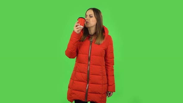 Lovely Girl in a Red Down Jacket Is Drinking Unpalatable Coffee and Is Disgusted. Green Screen