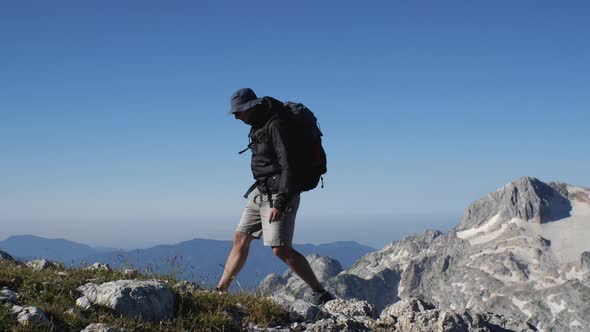 A man in shorts and a windbreaker with a backpack on his back is walking through the mountains again