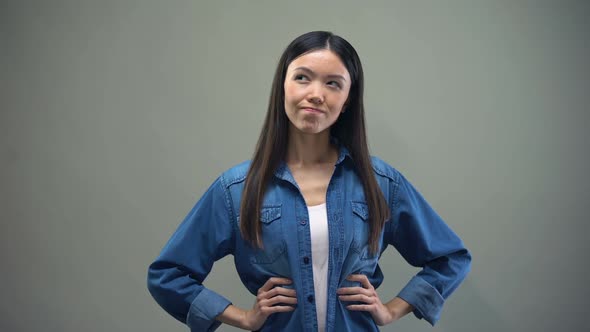 Asian Woman Standing on Grey Background, Making Choice Between Two Options