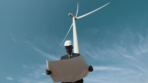 Man in Suit Standing Among Windmills with Blueprints