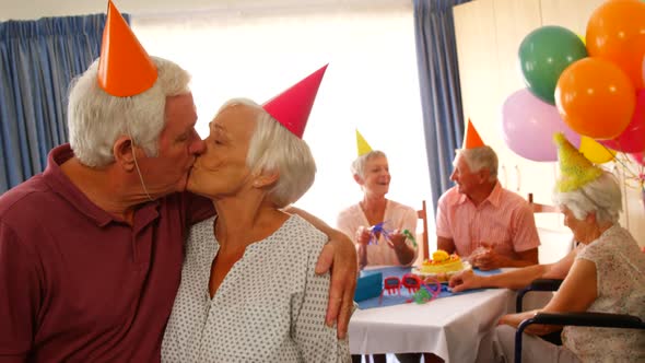 Senior couple kissing and hugging while celebrating birthday with friends