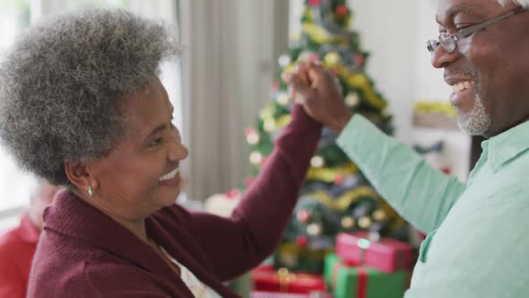 Happy african american senior couple dancing together with friends in background at christmas time