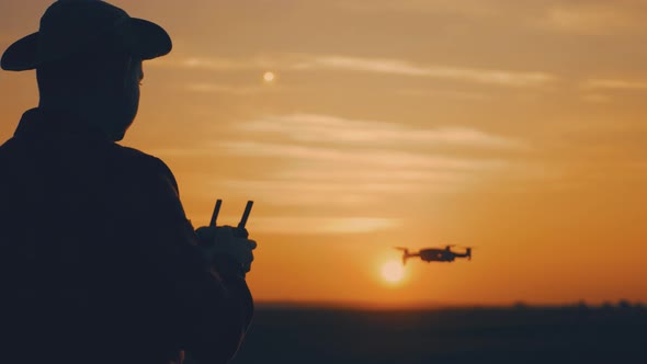 Silhouette of a Farmer Using a Drone in a Wheat Field at Sunset. Concept Technology Innovations for