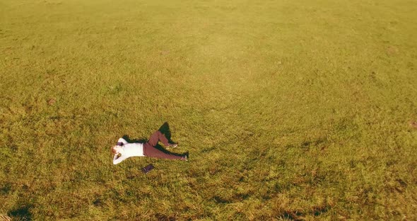 Low Orbital Flight Around Man on Green Grass with Notebook Pad at Yellow Rural Field.