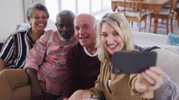 Two diverse senior couples sitting on a couch using a smartphone and taking a selfie