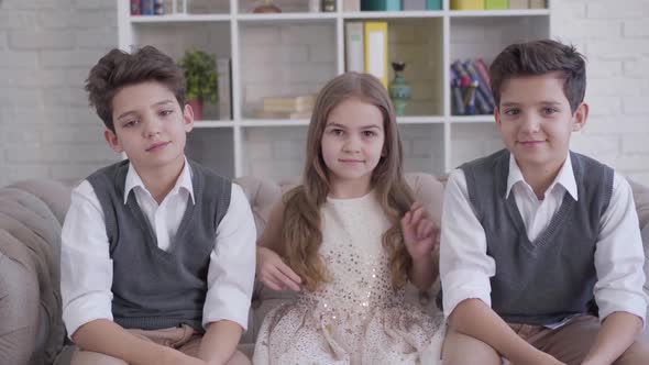 Portrait of Three Positive Caucasian Children Sitting on Couch and Showing Thumbs Up. Twin Brothers