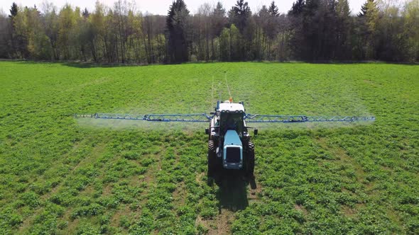 Aerial view of farming tractor spraying mineral, nitrogen fertilizer or pesticides